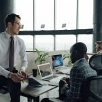 Three men engaged in a business meeting in a modern office setting with laptops and documents. — A New Player in Town: UFABET