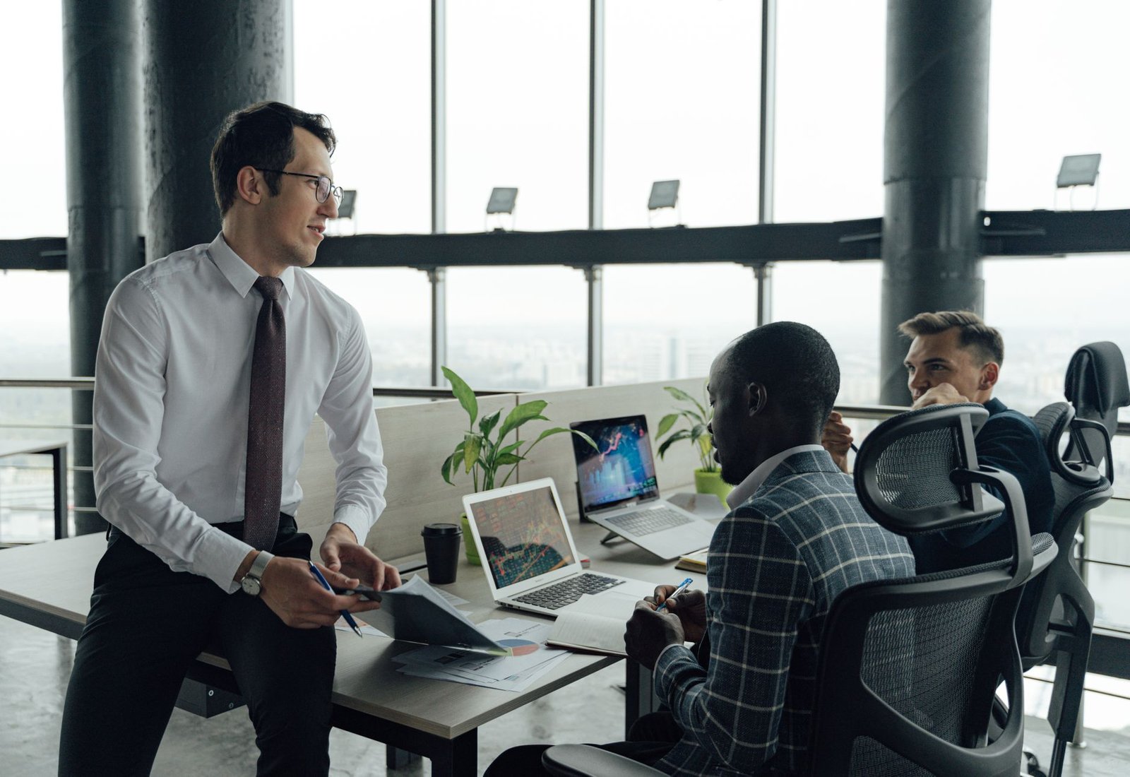 Three men engaged in a business meeting in a modern office setting with laptops and documents. — A New Player in Town: UFABET