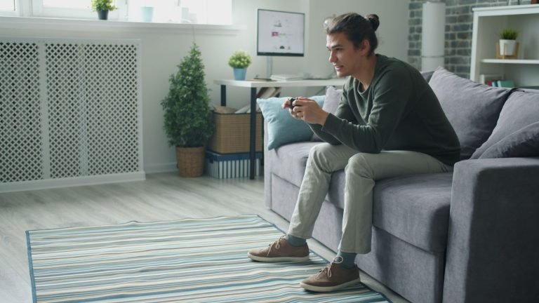 Smiling young man enjoying video games on a sofa at home. — Explore USA Casino Bonuses with Free Spins and Extra Chips Online