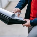 Close-up of a professional person reviewing documents outdoors. Engaged in work with focus on writing materials. — From Passi