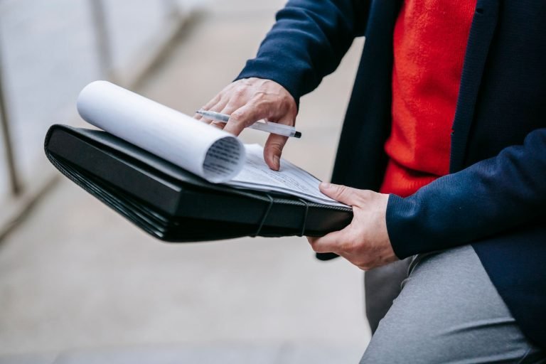 Close-up of a professional person reviewing documents outdoors. Engaged in work with focus on writing materials. — From Passi