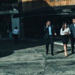 Three business professionals walk along a city street outside a cafe. — Navigating Employment Challenges in Entertainment Est