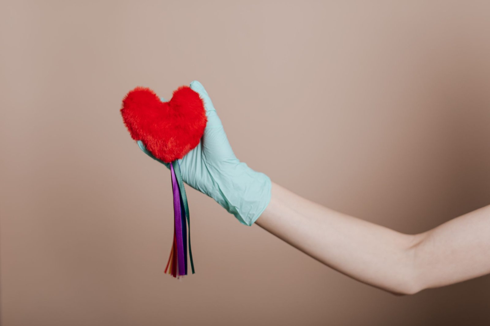 A latex-gloved hand holds a red heart-shaped plush with colorful strings, symbolizing love and safety. — Nuru massage near me