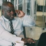 Professional man multitasking, talking on the phone while using a laptop in an office. — Quality Window Installation Services