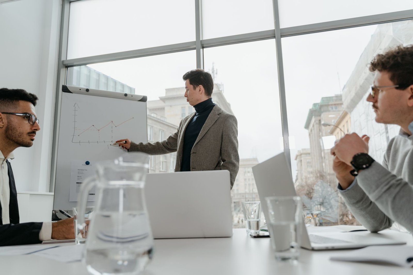 Professionals engaged in a collaborative business meeting with charts and laptops in a modern office setting. — The Benefits