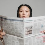 Asian woman with braided hair reading a newspaper in a studio setting. — Top Medicare Advantage Plans to Consider for 2026